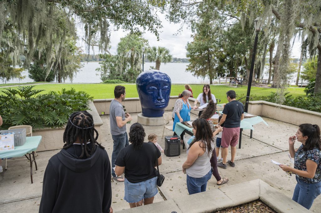 People interact on Rollins Museum of Art's back patio surrounding Kaneko's blue ceramic head sculpoture.