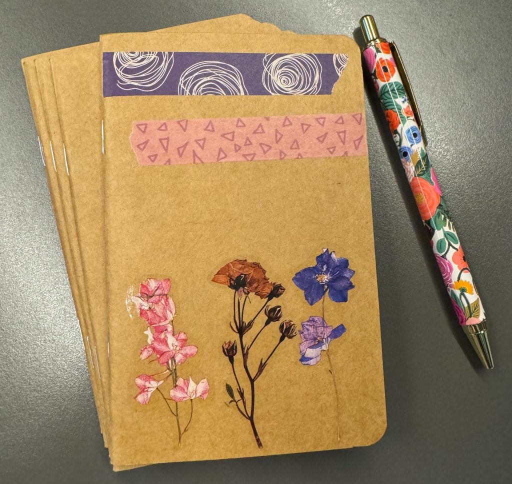 colorful pen lays beside a brown journal decoprated with flowers and colorful tape