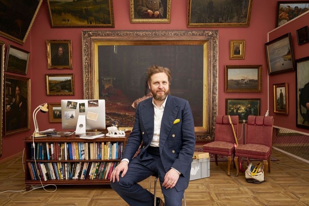 Ragnar Kjartansson sits in a gallery with red walls in front of a bookcase