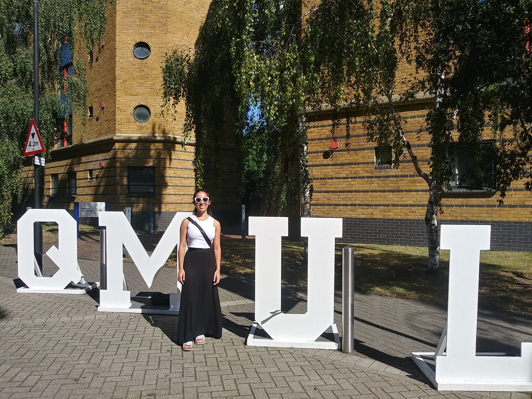 Carla stands outside in the middle of large letters spelling QMUL.