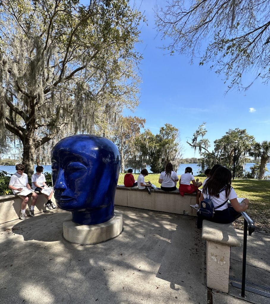 Students draw surrounding Jun Kaneko's blue ceramic head statue on Rollins Museum of Art's back patio.