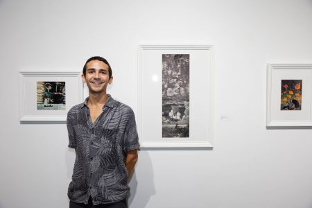 Man stands in front of artwork that is hung in a white art gallery