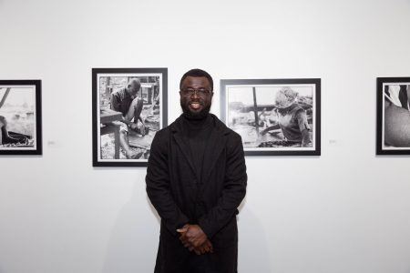 Samuel Aye-Gboyin Poses with his works on view at UCF Art Gallery, Photo: Jessica Abels